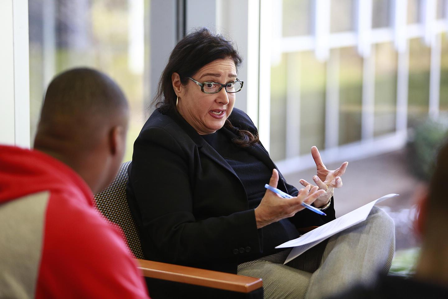 female with dark hair and glasses in black shirt, black blazer, gray pants; male in red and gray hooded sweatshirt